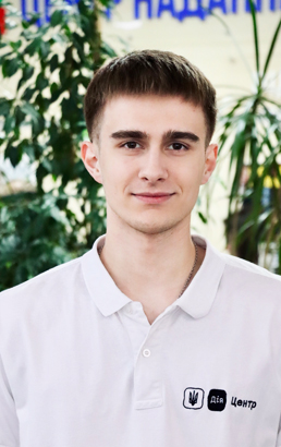 Молодий хлопець зі світло-русявою стрижкою у білій футболці . У приміщенні. Вираз доброзичливий.